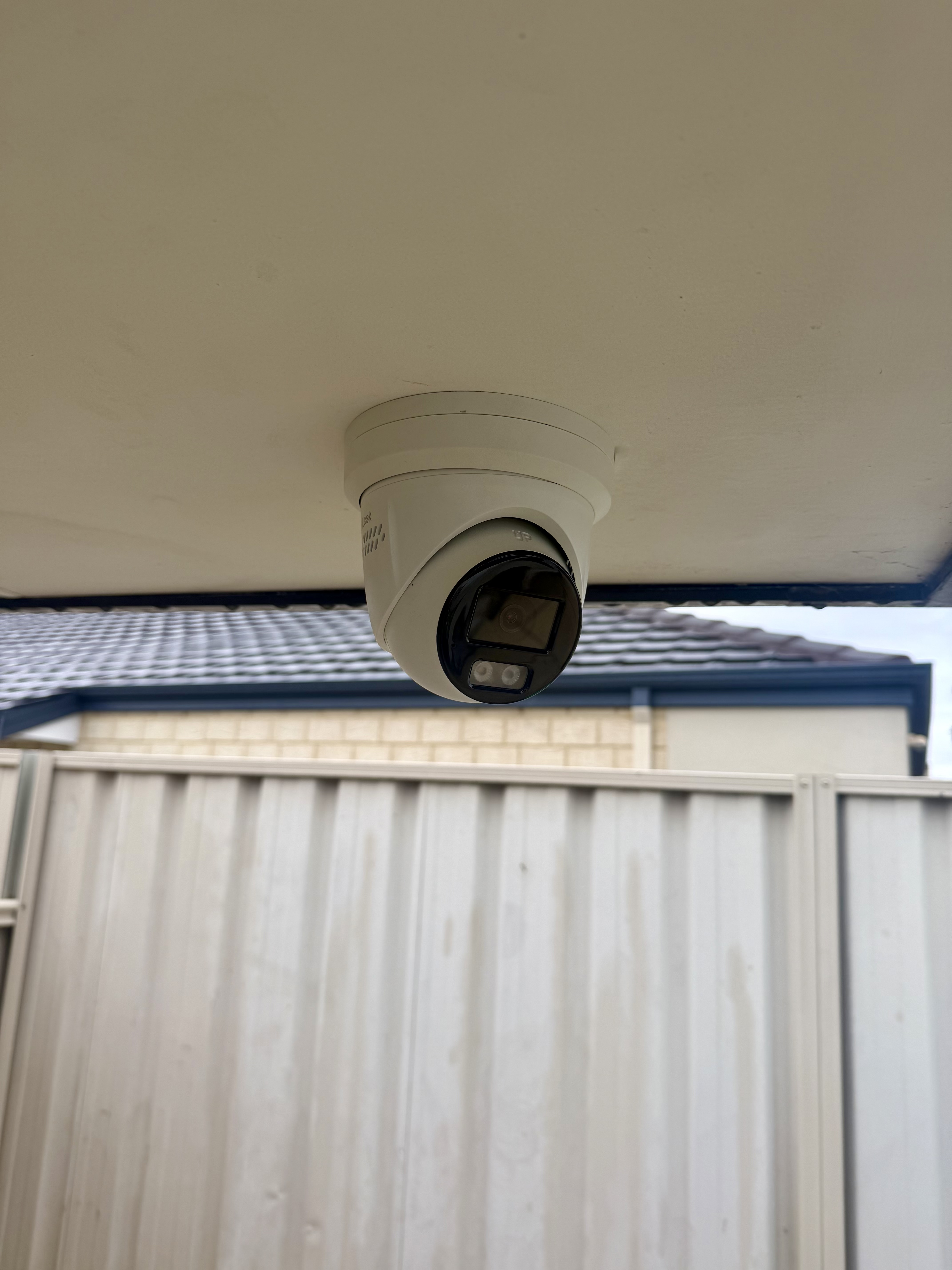Hikvision turret CCTV camera installed under eave, covering side access and rear yard