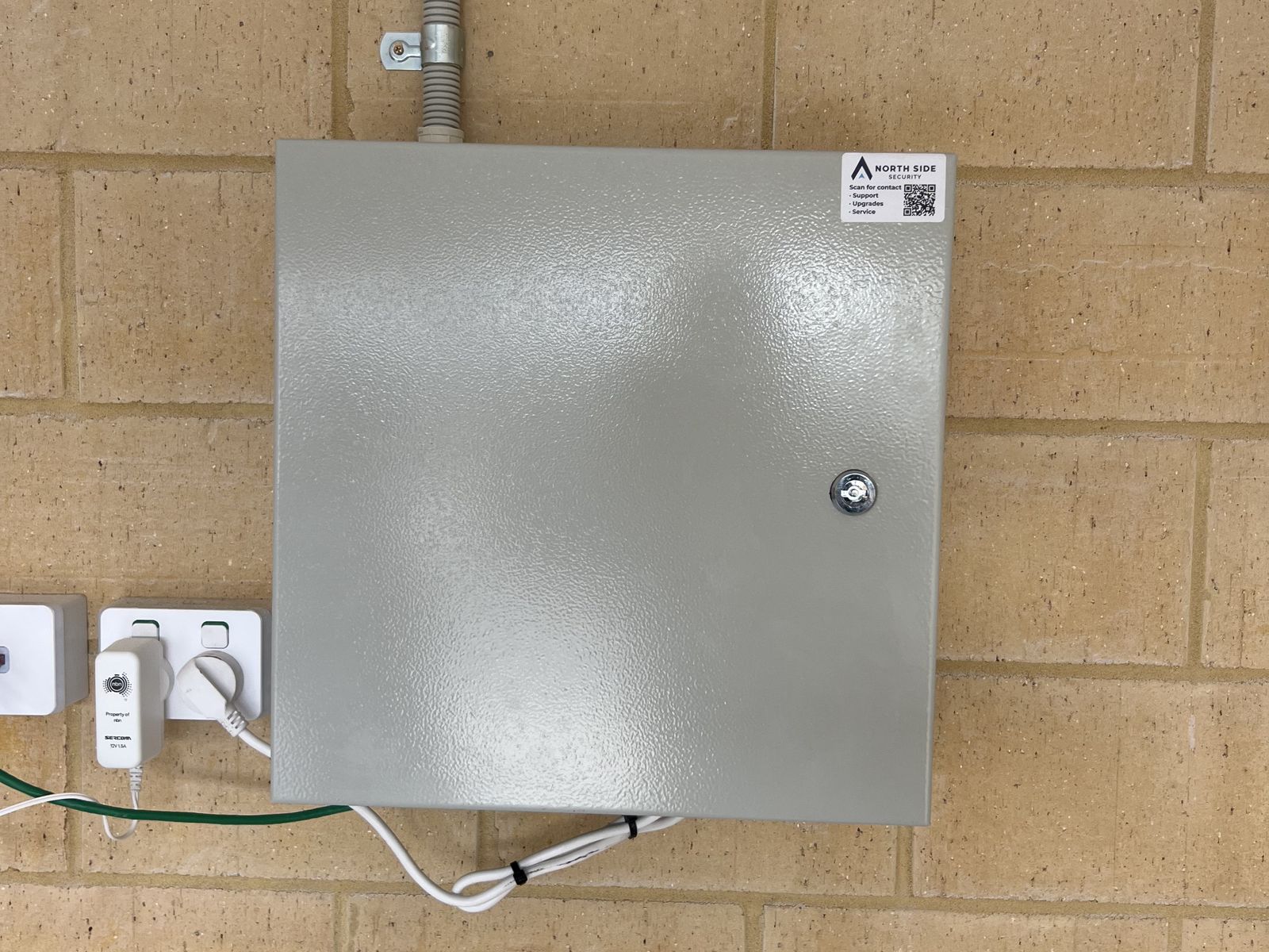 Lockable steel enclosure on a brick wall with a North Side Security service label